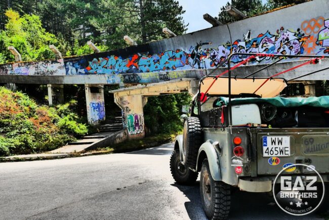 Zdjęcie przedstawia Gaza 69 na tle zniszczonego toru bobslejowego, który w 1984 roku wykorzystywany był podczas XIV Zimowych Igrzysk Olimpijskich w Sarajewie. Gaz 69 na tle toru bobslejowego w Sarajewie